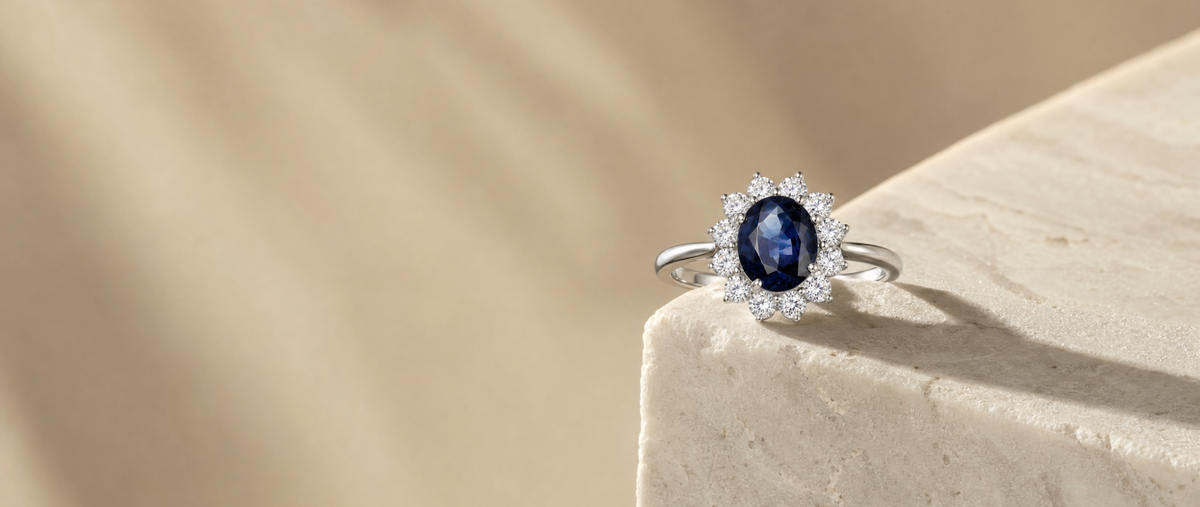 Anillo de oro con zafiro oval y halo de diamantes sobre superficie de mármol