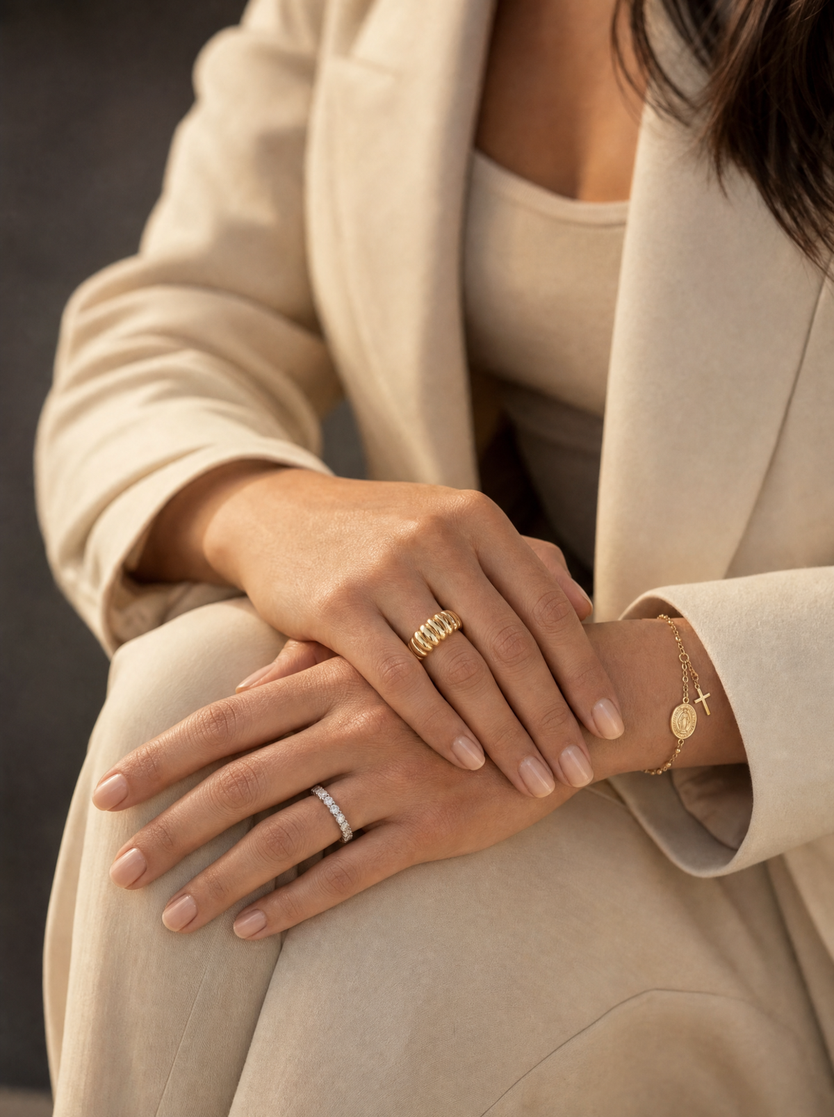 Manos con varios anillos de oro y una pulsera de rosario, en luz cálida natural